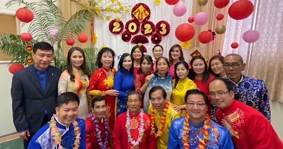 Members of the Marriage and Family Enrichment community in ao dai and leis posing in front of 2023 Lunar New Year decorations